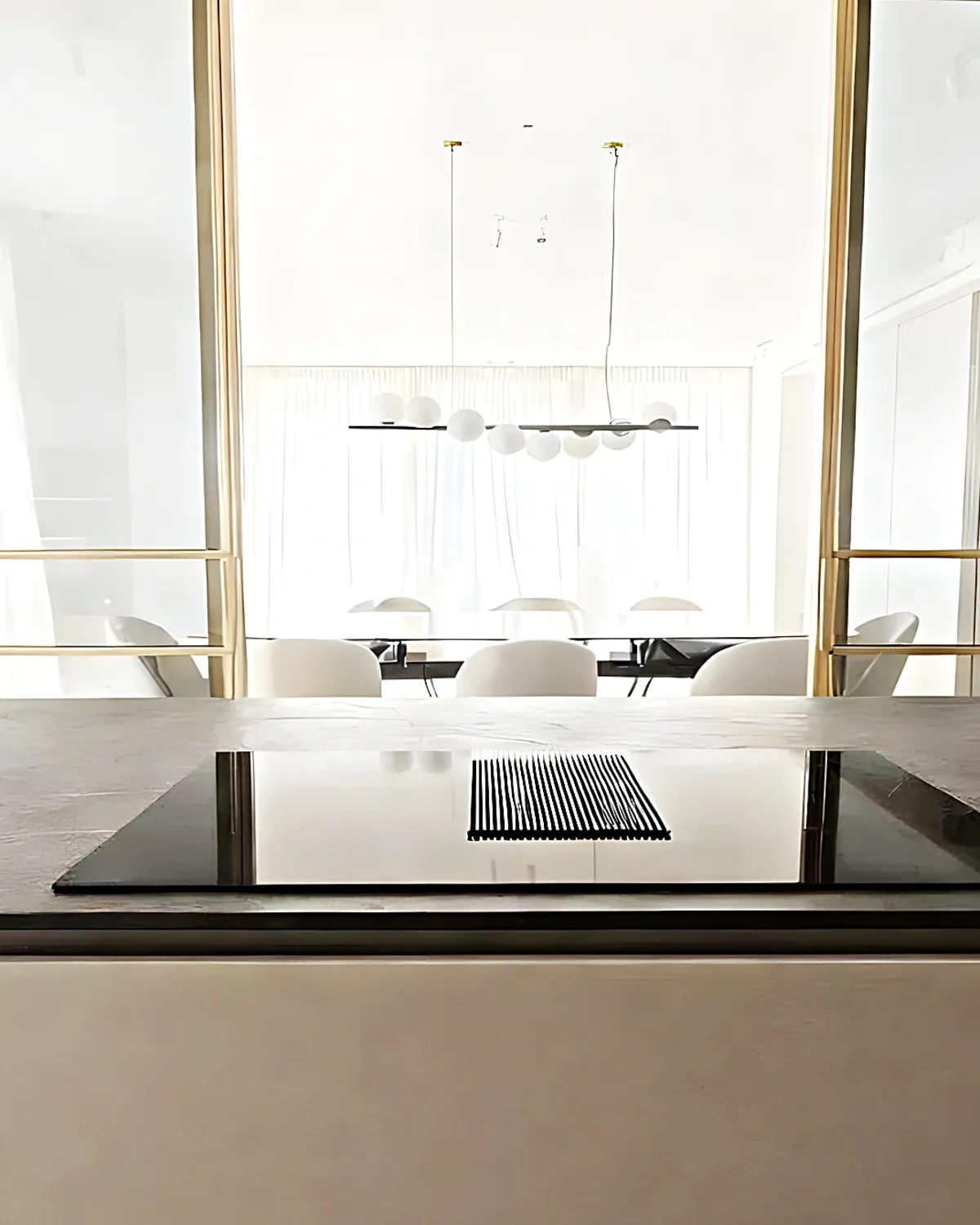 Kitchen island with integrated hob opening to the dining room through brass-framed glass doors, Vilanova