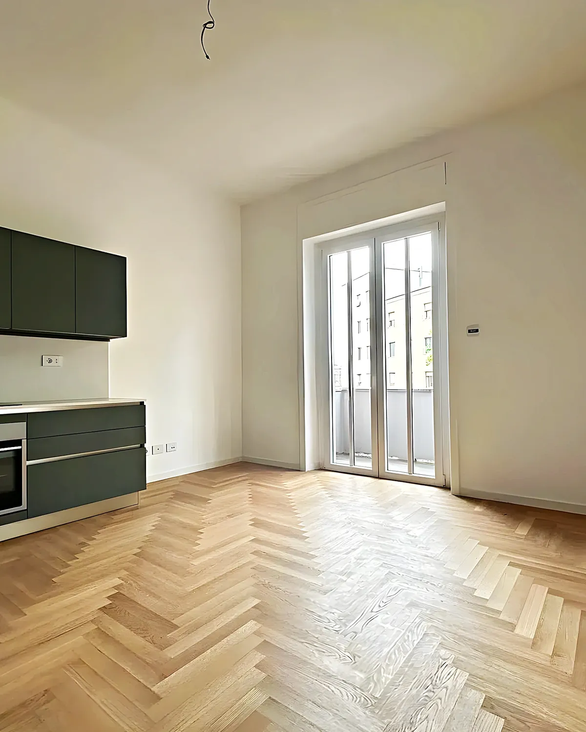 Open olive-green kitchen with herringbone parquet in a renovated Les Roquetes apartment